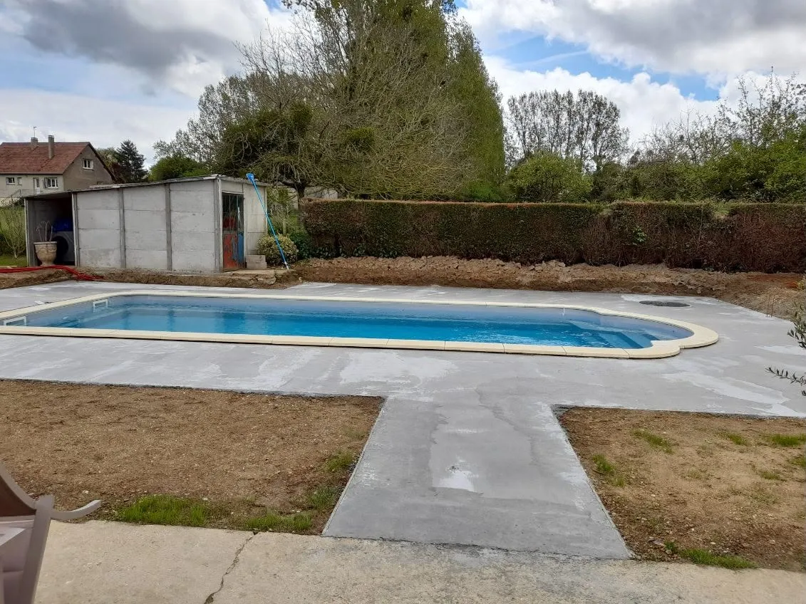 Piscine et sa plage en béton, allée d’accès dans le jardin